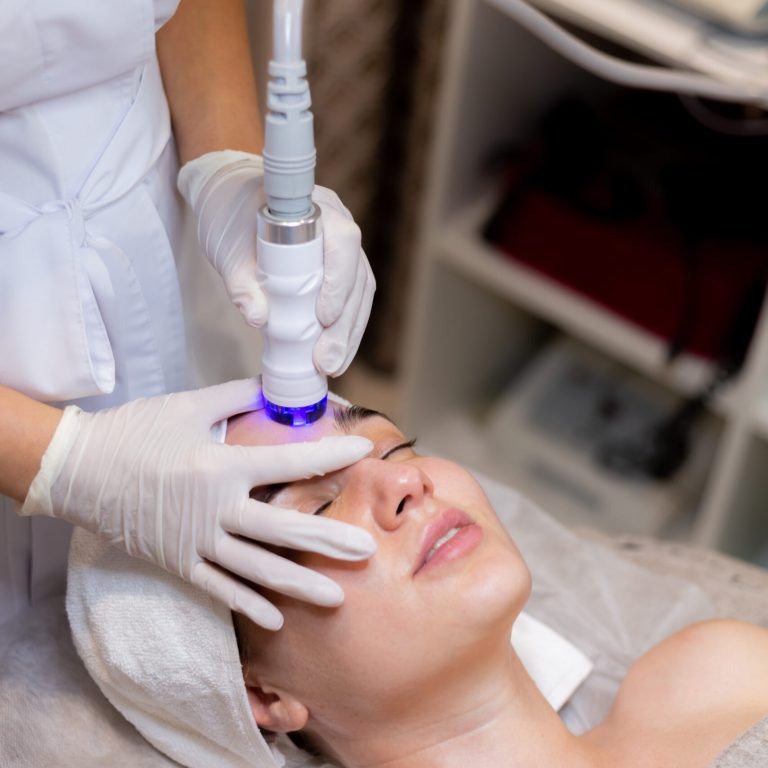 A young beautiful girl lies on the beautician's table and receives procedures with a professional apparatus for skin rejuvenation and moisturizing