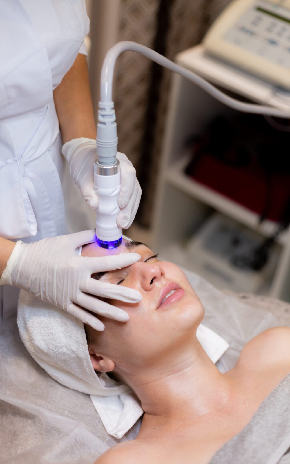 A young beautiful girl lies on the beautician's table and receives procedures with a professional apparatus for skin rejuvenation and moisturizing